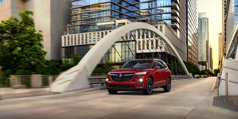 Brand new red 2023 Buick Enclave driving down city streets.