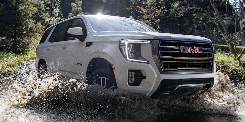 Brand new white 2023 GMC Yukon driving off road through a body of water.