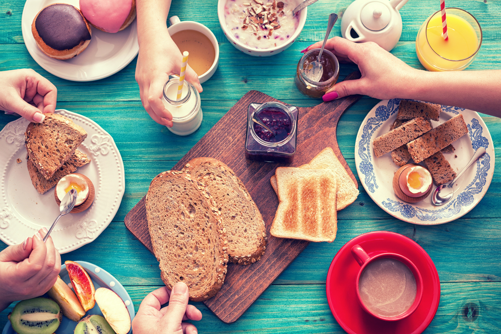 Areal view of a variety of breakfast items on a table with 4 people eating from the spread.