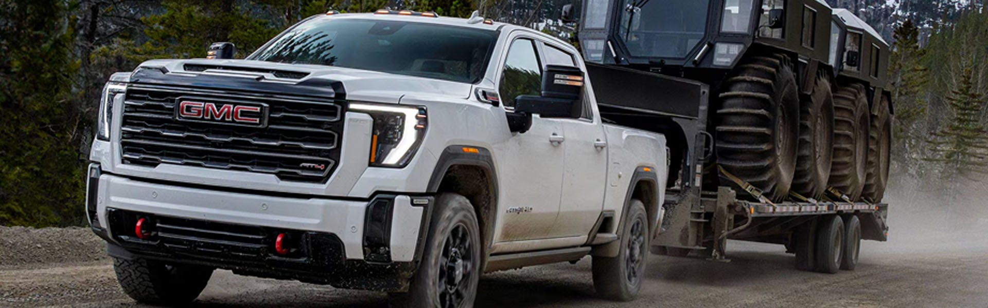 White 2026 GMC Sierra 3500HD towing a heavy tracked trailer on a gravel road