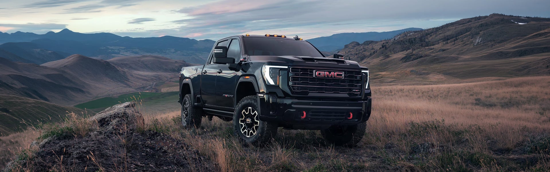 Black 2026 GMC Sierra 3500HD parked on a mountain ridge at dusk, front three-quarter view
