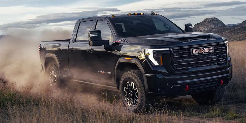 Black 2026 GMC Sierra 3500HD AT4 driving through tall grass, dust trailing behind