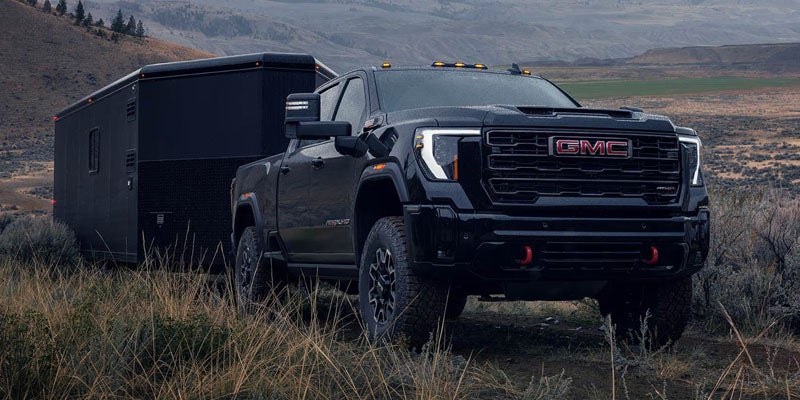 Black 2026 GMC Sierra 3500HD towing a camper trailer through desert terrain