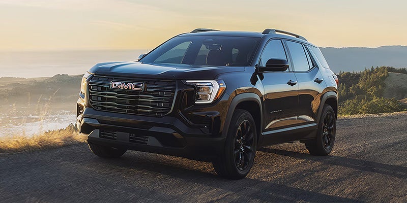 A black 2027 GMC Terrain on a hillside at sunset, front three-quarter view