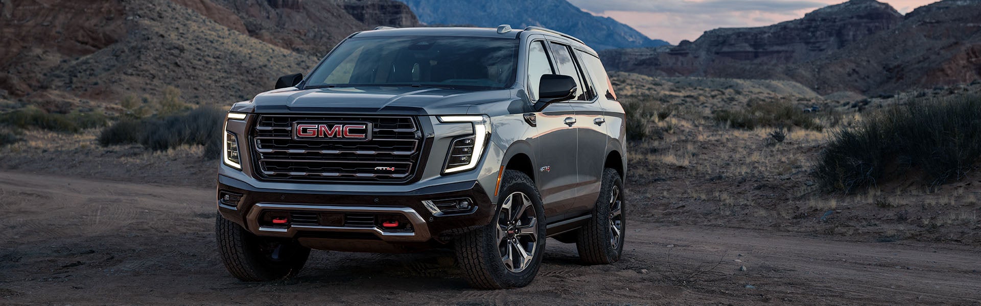 2027 GMC Yukon AT4 parked on a desert trail at dusk, front three-quarter view