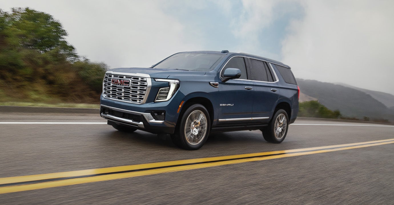 2027 GMC Yukon Denali driving on a mountain road, blue exterior, front three-quarter view