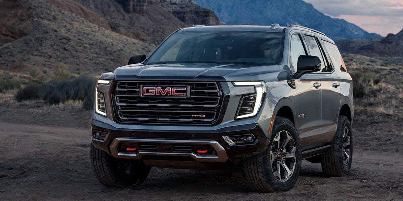 2027 GMC Yukon AT4 parked on a desert trail, silver exterior, front three-quarter view