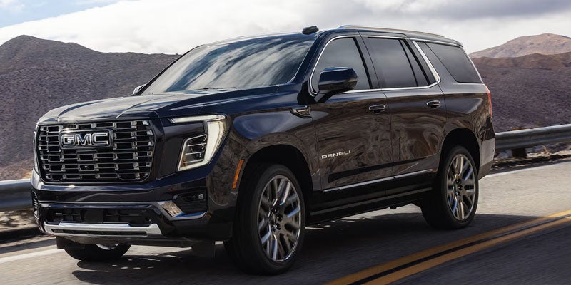 2027 GMC Yukon Denali driving on a mountain road, front three-quarter exterior view